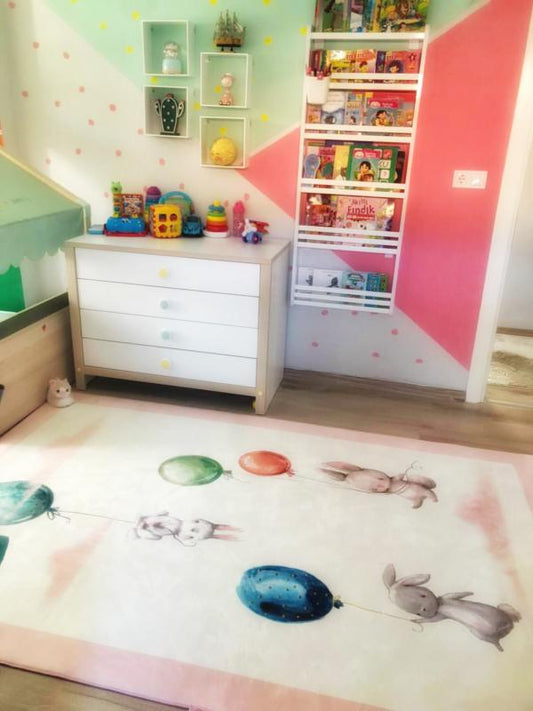 Çocuk odasında pembe zemin halısı, balon tutan sevimli tavşanlar ile dekore edilmiş.