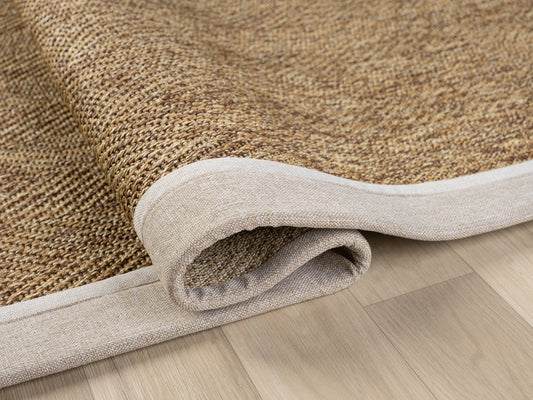 Sisal halının kenarı, yuvarlanmış halde ve el yapımı kumaş bordürü ile görünür.