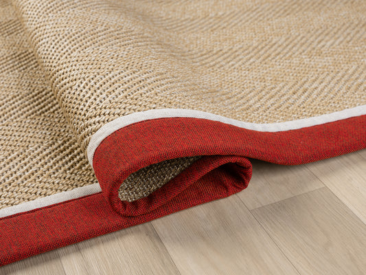 Kırmızı kumaş bordürlü sisal halının hafifçe katlanmış hali, doğal dokulu tasarımıyla dikkat çekiyor.