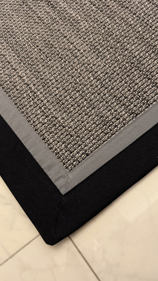 Gri Kumaş Bordürlü Sisal Halı, dayanıklı ve şık tasarımıyla ev dekorasyonuna modern bir dokunuş katıyor.