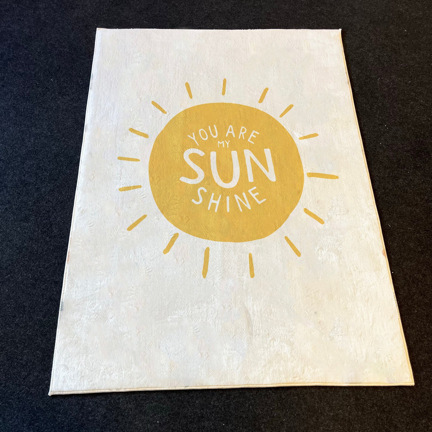 Beyaz zemin üzerinde sarı güneş ve 'You Are My Sunshine' yazısı bulunan çocuk halısı, hem oyuncakların hem de çocukların oyun alanı için mükemmel bir seçim.