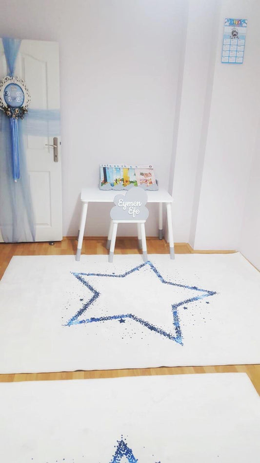 Beyaz bir odada lacivert yıldızlı halının serildiği, şık bir masa ve dekoratif aksesuarlarla dolu çocuk odası.