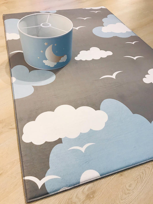 Bulut deseniyle tasarlanmış mavi çocuk odası halısı, üstünde yuvarlak bir sepet ile birlikte gösteriliyor.