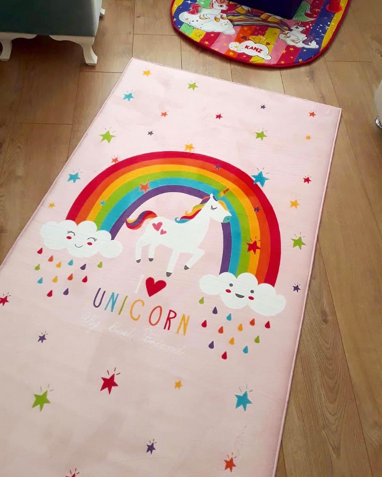 Pembe renkli unicorn temalı çocuk odası halısı, gökyüzünde bulutlar ve yağmur damlaları ile süslenmiş, arka planda bir rainbow deseni bulunuyor.