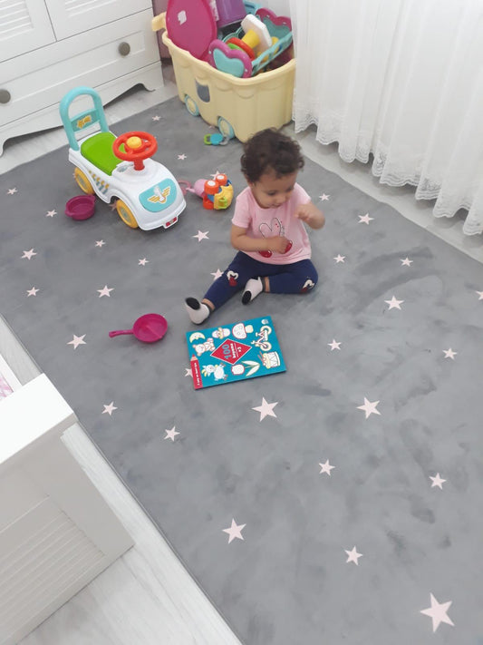 Gri çocuk odası halısının üzerinde oturan bir çocuk, etrafında oyuncaklar ve bir mini araba var. Oda aydınlık ve çocuklar için eğlenceli bir alan sunuyor.