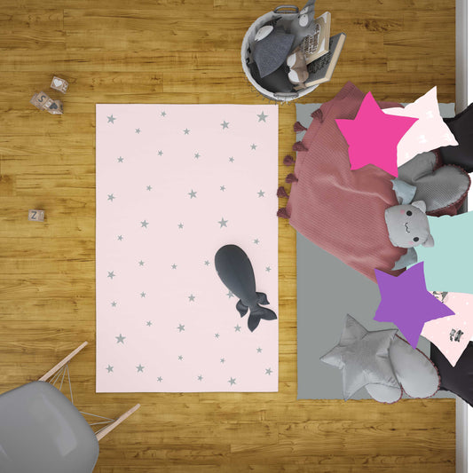 Kahverengi zemin üzerinde yıldız desenli pembe halı, etrafında oyuncaklar ve yastıklarla dolu bir çocuk oyun alanı. Rahat bir oyun alanı sunuyor.