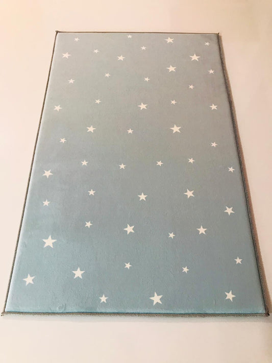 Beyaz yıldızlarla süslü açık mavi çocuk halısının genel görünümü, modern ve şık bir dekorasyon unsuru.
