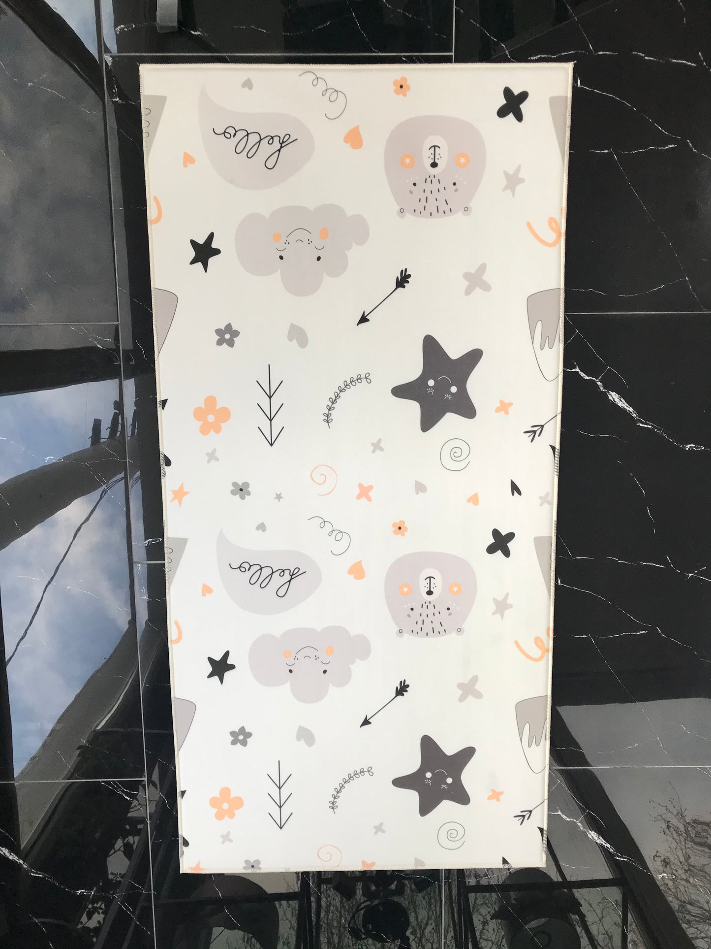 Halıdan yukarıdan görünüm, çeşitli sevimli figürlerin yer aldığı desenler ile dolu. Arka planda modern bir iç mekan görünümü.