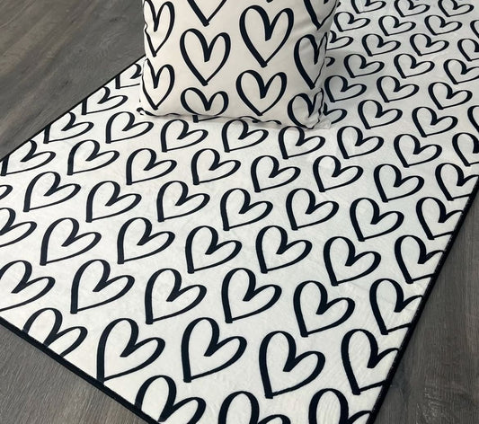 Şık siyah-beyaz kalp desenli halının üzerinde yastık, çocuk odası dekorasyonunu tamamlamak için mükemmel bir seçenek.