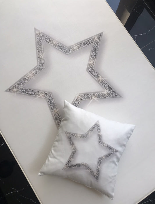 Aynı gümüş yıldız desenli halı ve yastık, farklı bir açıdan gösterilerek zarif tasarımı vurgulanıyor. Düz beyaz zemin ile kontrast oluşturan modern bir dekorasyon unsuru.