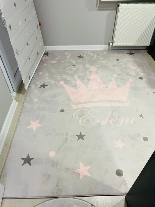 Gri zemin üzerine pembe ve gri yıldızlarla süslü prenses taçlı halının bulunduğu modern bir iç mekan.