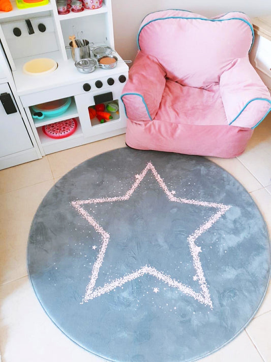 Yuvarlak gri yıldızlı halı, pembe bir çocuk koltuğu ile birlikte bir oyun alanında yer almakta. Renkli oyun seti ve dekoratif öğelerle neşeli bir ortam oluşturuyor.