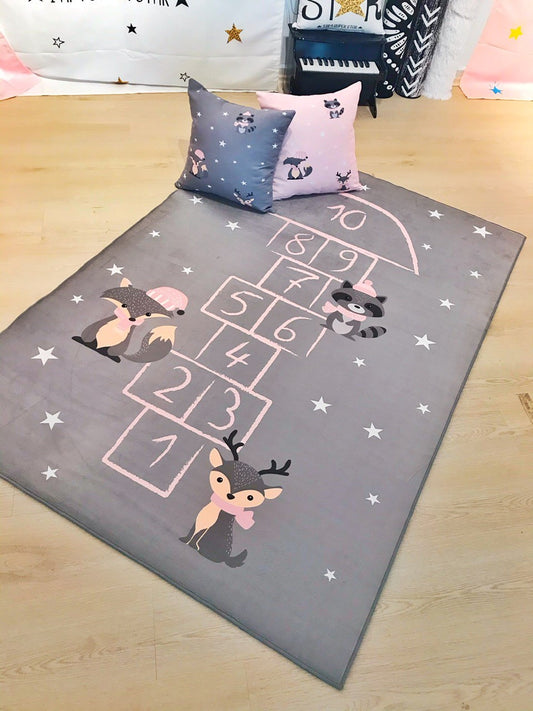 Yumuşak gri çocuk odası halısı, zıplama oyunu deseni ile birlikte, sevimli hayvan figürleri ve yastıklarla dekore edilmiş bir alan.