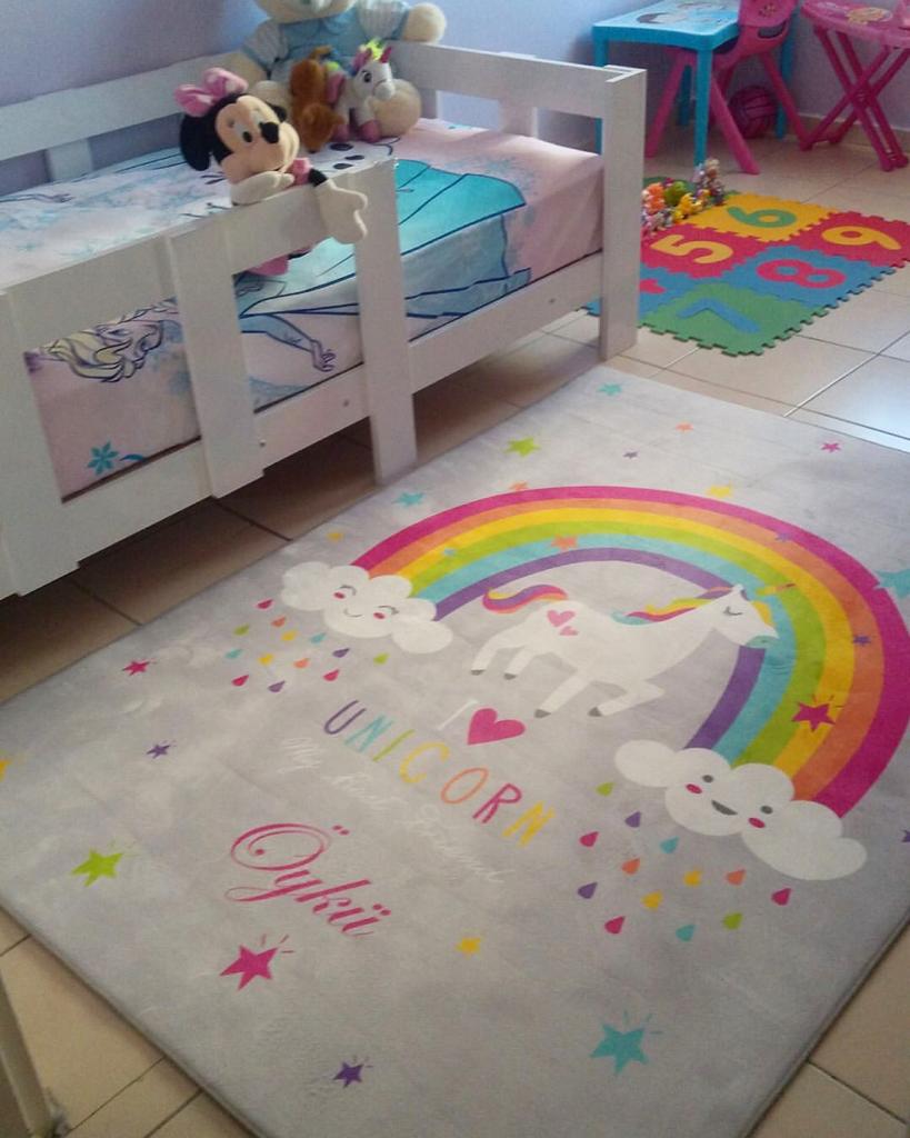 Çocuk odasında bulunan unicorn desenli halı, yanında oyuncaklarla dolu bir yatak.