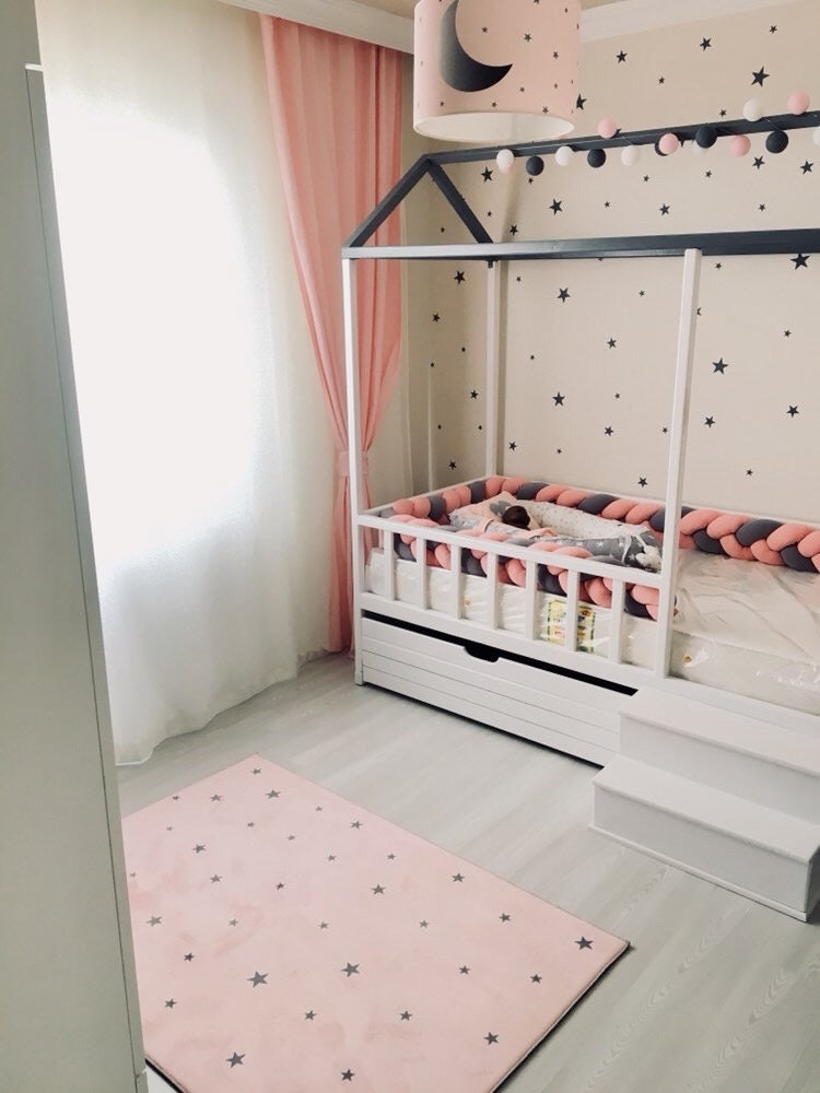 Yıldız deseni olan pembe çocuk odası halısı, modern bir bebek odasında yer alıyor. Odanın pastel tonları, döşemeleri ve ışıklarla uyum sağlıyor.