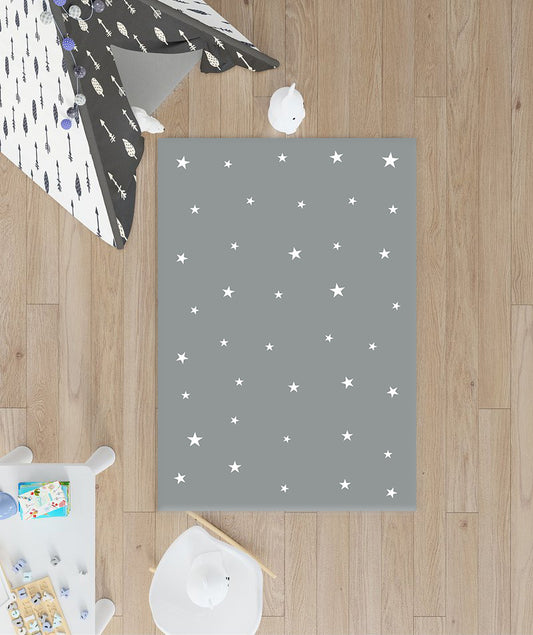 Ahşap zemin üzerinde yer alan gri yıldızlı halı, etrafında oyuncaklar ve çocuk masası bulunan bir oyun alanı.