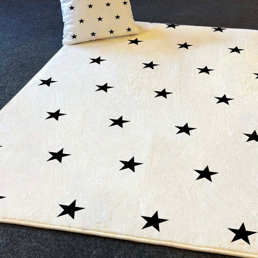 Siyah yıldızlarla kaplı beyaz bir halı ve arka planda yer alan yastık, modern bir oyun alanına hoş bir dokunuş katıyor.