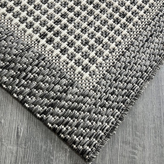 Jüt sisal halının köşeden çekilmiş görüntüsü, siyah ve beyaz dokusu ile modern bir görünüm sunuyor.