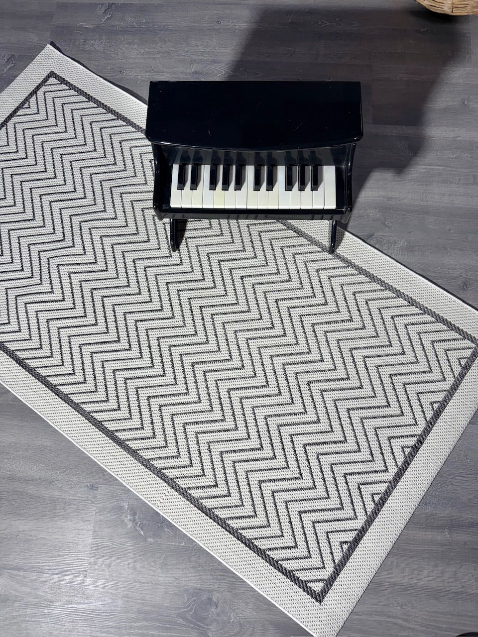 Halı Vagonu JS9718 jüt sisal halı, zigzag desenli antrasit beyaz. Halının üstünde küçük bir piyano yer alıyor.