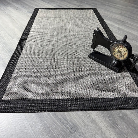 Gri-siyah jüt sisal halının geniş açılı görüntüsü, yanında vintage bir dikiş makinesi yer almakta.