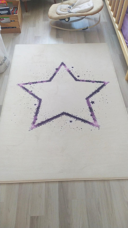 Mor yıldız deseniyle tasarlanmış çocuk odası halısı, ahşap zemin üzerinde görünmekte. Halının etrafında çocuk mobilyası ve oyuncaklar yer almakta.
