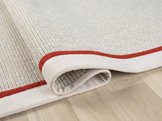 Kırmızı kumaş bordürlü el yapımı sisal halının rüzgarda hafifçe kıvrılmış görünümü, modern bir tarzı yansıtıyor.