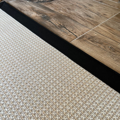 HALI VAGONU Siyah Krem Kumaş Bordürlü Sisal Halı - El yapımı, dayanıklı, modern tasarım. Halının kenarında siyah kumaş bordürü dikkat çekerken, ahşap zemine konumlandırılmış durumda. Krem sisal halı, evdeki her alan için şık ve güvenilir bir seçim. Yüksek kaliteli, kolay temizlenebilir halı, el yapımı özellikleriyle ev dekorunu zenginleştirir.