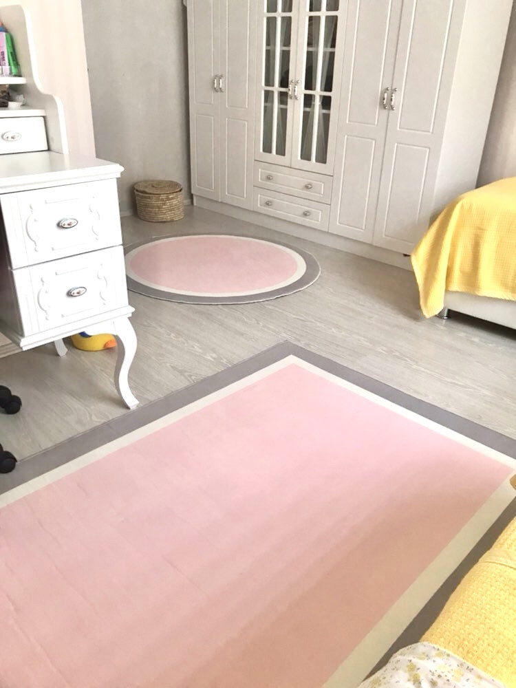Yumuşak gri pembe tasarımlı çocuk halısı, beyaz dolap ve masa ile dekore edilmiş bir odada yer alıyor.