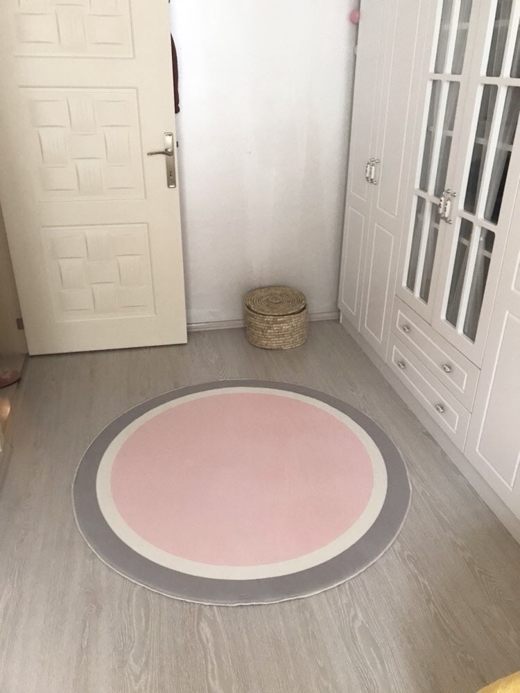 Bir odanın ortasında yuvarlak bir halı, gri ve pembe renk kombinasyonuyla sade bir dekor oluşturuyor.