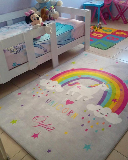 Çocuk odasında bulunan unicorn desenli halı, yanında oyuncaklarla dolu bir yatak.