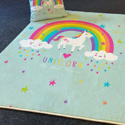 Gökkuşağı ve unicorn tasarımına sahip çocuk odası halısı, yanına yerleştirilmiş yastık ile birlikte, koyu bir zemin üzerinde serili.