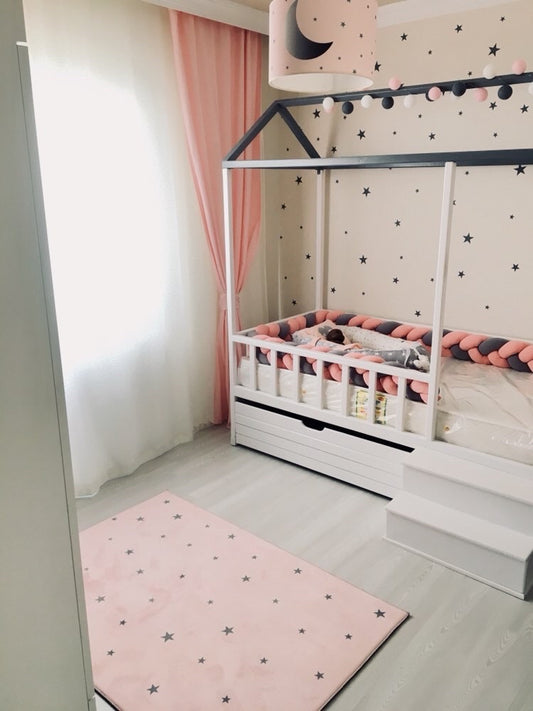 Yıldız deseni olan pembe çocuk odası halısı, modern bir bebek odasında yer alıyor. Odanın pastel tonları, döşemeleri ve ışıklarla uyum sağlıyor.