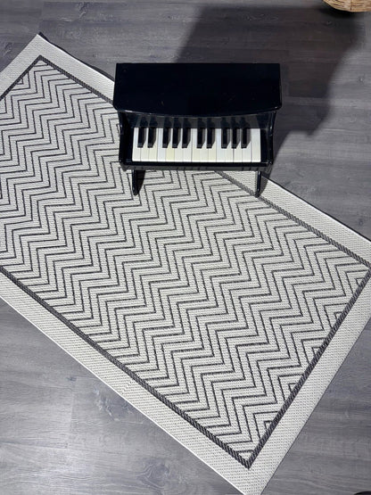 Halı Vagonu JS9718 jüt sisal halı, zigzag desenli antrasit beyaz. Halının üstünde küçük bir piyano yer alıyor.