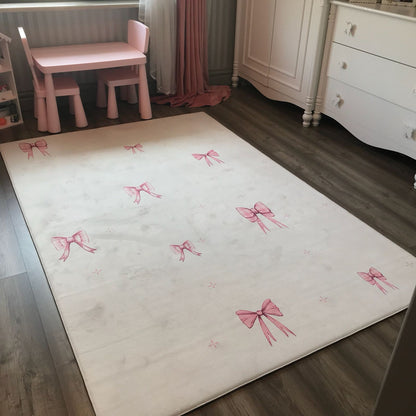 Pembe fiyonk desenli çocuk halısı, odanın dekorasyonuna şıklık katıyor. Arka planda pembe mobilyalar bulunuyor.