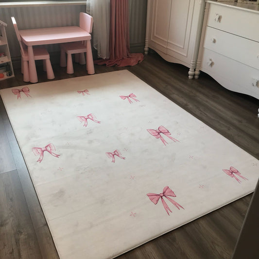 Pembe fiyonk desenli çocuk halısı, odanın dekorasyonuna şıklık katıyor. Arka planda pembe mobilyalar bulunuyor.
