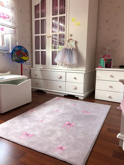 Çocuk odasında pembe fiyonk desenli yumuşak halı, şık mobilyalarla uyum içinde.