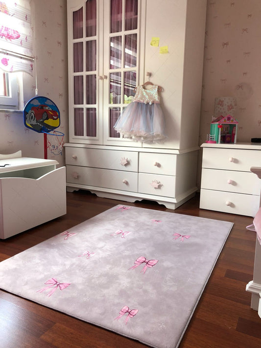 Çocuk odasında pembe fiyonk desenli yumuşak halı, şık mobilyalarla uyum içinde.